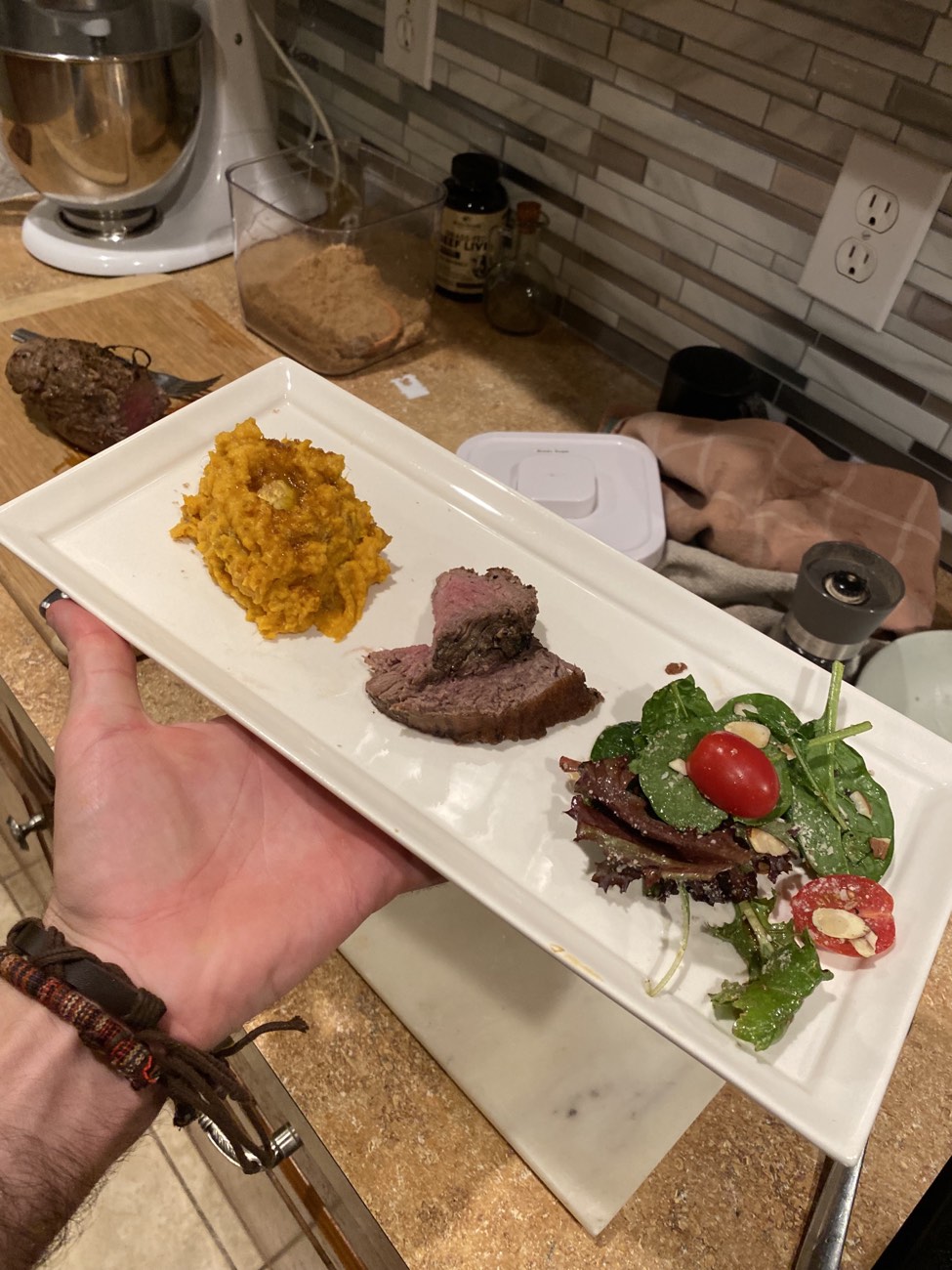 A plated steak with sweet potato and a spinach salad, held on a white platter.