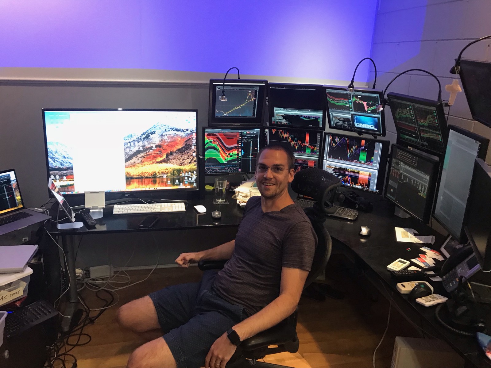 David at a desk backed by a wall of ten monitors running live charts.