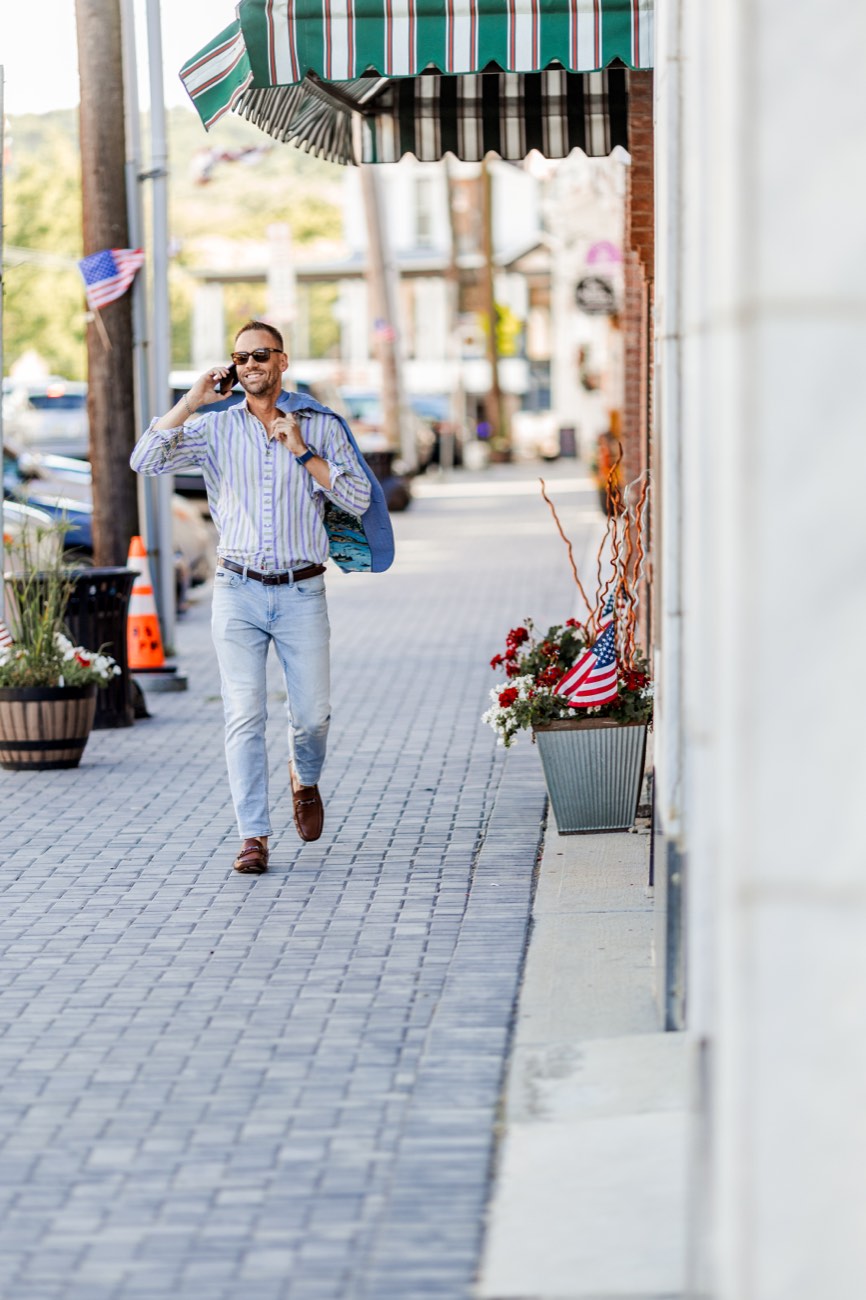 David walking a small-town main street past a striped awning and storefronts.
