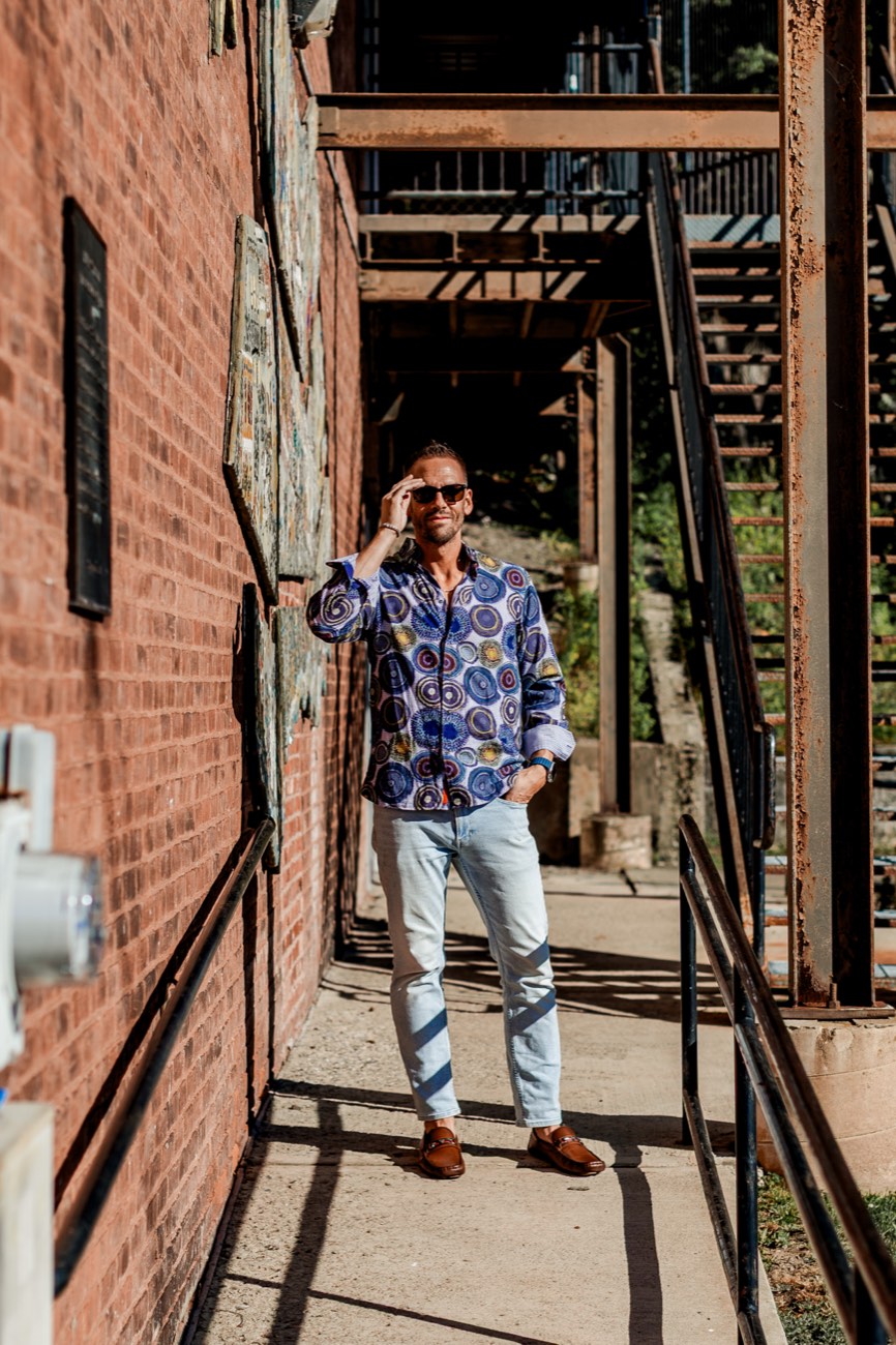 David in a boldly patterned shirt in a brick alleyway.