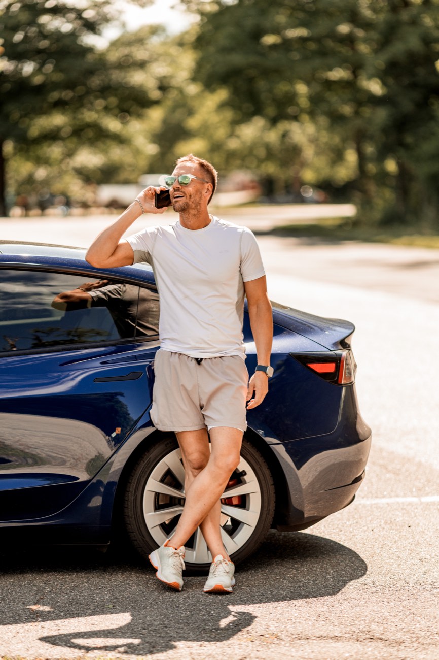 David leaning against a blue Tesla, on the phone.